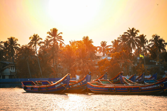 View of traditional fishing boats, adorned with vibrant blue hues, gently bob on the tranquil waters under a golden sunset, Kochi, Kerala, India.