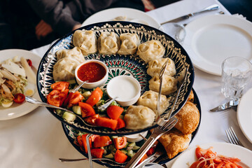 Manty and chebureki on table in cozy restaurant with people.