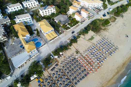 Aerial view of the beach umbrellas lining the shore, contrasting with the buildings and the calm, clear waters of the sea, Paralia, Preveza, Greece.