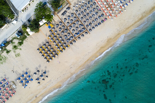 Aerial view of neatly arranged beach umbrellas casting shadows on the golden sands where the turquoise sea meets the shore, Paralia, Preveza, Greece.