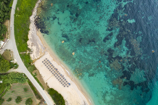 Aerial view of azure waters meet the sandy shore where beach umbrellas stand in organized rows, a scene of coastal serenity, Paralia, Preveza, Greece.