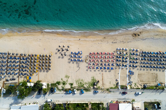 Aerial view of sun umbrellas dotting the sandy beach where the turquoise sea meets the shore, Paralia, Preveza, Greece.