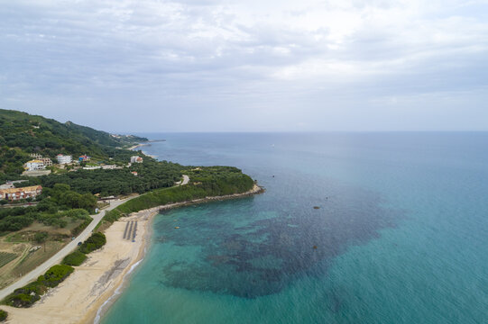 Aerial view of the turquoise sea gently kissing the sandy shore, where the lush green hills meet the azure horizon, Paralia, Preveza, Greece.