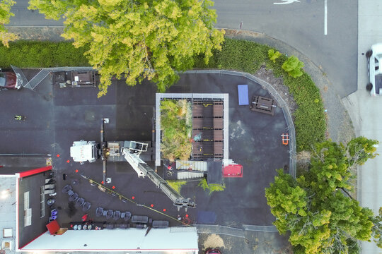 Aerial view of a crane lifting a tree over a building contrasting the dark asphalt and vibrant green foliage, Quantum Assembly, Portland, United States.