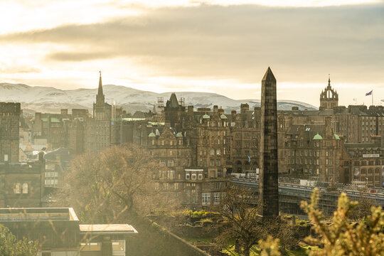 View of ancient obelisk standing tall amidst the vibrant cityscape, where historic buildings meet modern life under a sky painted with golden light, Edinburgh, Scotland, United Kingdom.