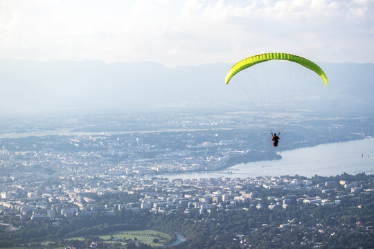 View of a paraglider soars high above the cityscape with its vibrant green canopy contrasting against the hazy horizon, Geneva, Geneva, Switzerland.