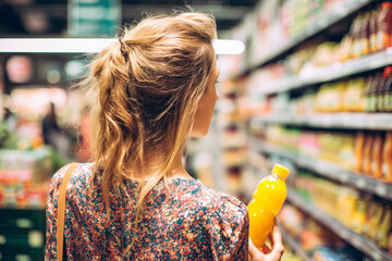 back view of young woman looking at bottle of juice in grocery store