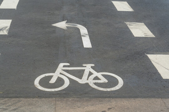 View of a white bicycle symbol and a left-turn arrow painted on the dark asphalt of a bike lane create a stark contrast, Indre By, Denmark.