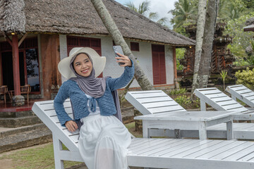 a young woman holding a cell phone in a hotel with a beach view while on vacation, perfect for vacation promotions and social media, holiday season.