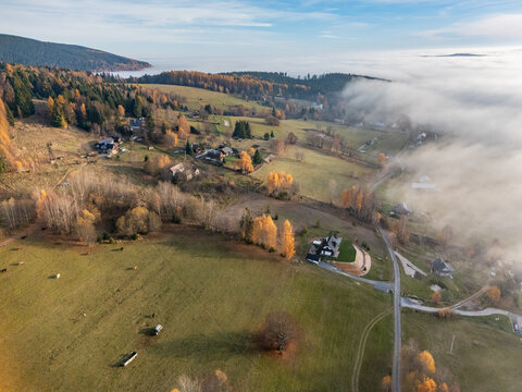 Aerial view of golden autumn hues blanketing rolling hillsides, meeting a soft, ethereal mist in the valley, Bratkovica, Detvianska Huta, Banskobystricky kraj, Slovakia.