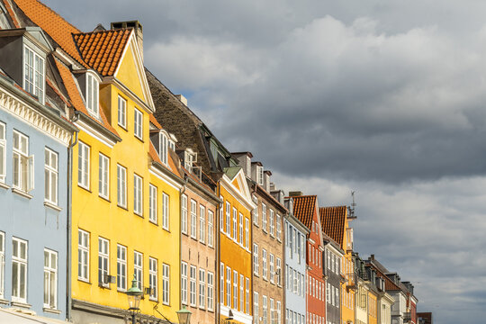 View of vibrant, colorful buildings stand in a row beneath a dramatic sky, their windows reflecting the light in Nyhavn, Copenhagen, Denmark.