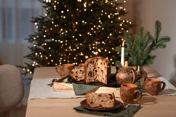 Christmas eve, festive holiday table with food, lifestyle home interior decor with blurred Christmas tree lights. Panettone, tea cups on table with linen napkins, Christmas or New Year holiday feast