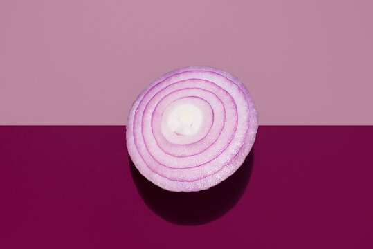 Una Cebolla roja cruda cortada por la mitad sobre un fondo rosa y granate. Vista superior
