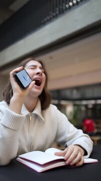 Vertical screen Young female student sits with notes in distress speaking to smartphone after ChatGPT mistake realizing she may fail studies feeling fear pressure and emotional breakdown