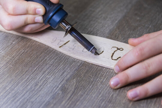 A childs hand writes by burning wood, pyrographic New Years text 2025/26