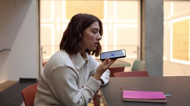 ChatGPT provides voice consultation to a focused office worker as she speaks into smartphone and listens to answers while sitting at table during calm modern work break