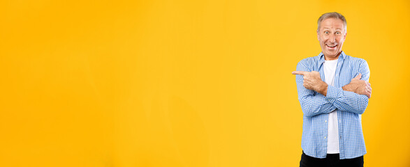 A man stands with arms crossed and a smile on his face. He points to the side in front of a bright yellow background. The scene shows his happy expression and casual clothing.