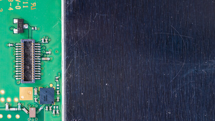 Macro of green circuit board with electronic components beside brushed metal surface, high tech engineering background with large copy space for text or interface design.