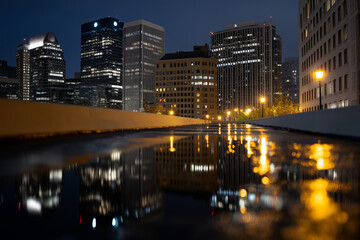 Naklejka premium A stunning urban skyline is beautifully illuminated at night, with reflections on wet streets capturing the essence of city life, vibrancy, and modern architecture.