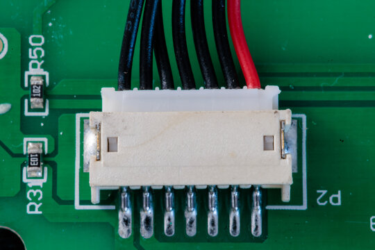Macro of white connector on green circuit board with blurred black and red wires, electronics background symbolising power, data and modern technology connections. - Powered by Adobe