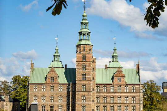 View of the Rosenborg Castle facade, showcasing its brickwork, green oxidized copper roofs, and spires against a blue sky, Copenhagen, Denmark.
