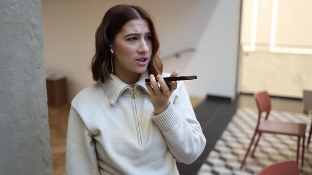 Young woman speaks angrily on smartphone expressing frustration and dissatisfaction tense face emotional tone heated phone conversation indoors modern stress moment