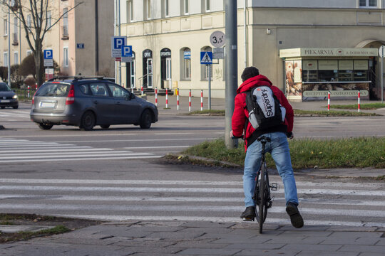 Kielce, Polska. 15.12.2025 - Rowerzysta w czerwonej kurtce przejeżdżający przez przejście dla pieszych na miejskim skrzyżowaniu.