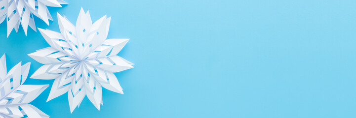 White snowflake shapes created from paper on light blue table background. Pastel color. Closeup. Handmade decoration elements for winter festive. Wide banner. Empty place for text. Top down view.