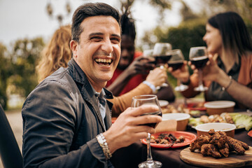 Smiling man enjoying outdoor dinner with friends during a cheerful wine toast