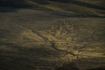 View of an arid landscape with a snaking road cutting through the terrain, bathed in the golden hues of setting sun, Latacunga, Cotopaxi, Ecuador.
