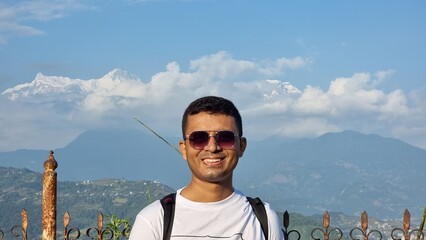 Smiling young man enjoying a magnificent mountain panorama, with snow-capped peaks and clear blue sky in the background, symbolizing adventurous travel and joyful exploration