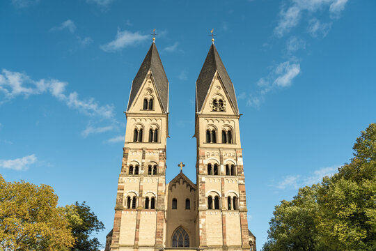 View of Basilica of St. Castor church with twin spires reaching towards the clear blue sky, framed by lush green trees, Koblenz Mitte, Rhineland-Palatinate, Germany.