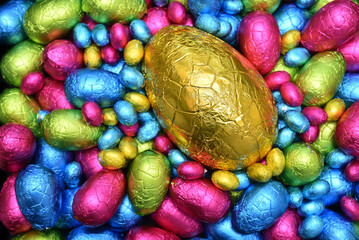 Pile  of colourful foil wrapped chocolate easter eggs in pink, blue, yellow and lime green with a large gold egg in the middle.