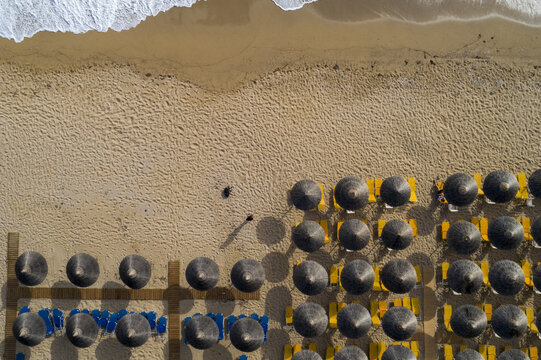 Aerial view of the beach with waves crashing near the sandy shore and rows of beach umbrellas, Vrachos, Preveza, Greece.