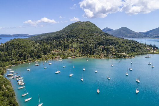 Aerial view of boats dotting the turquoise bay against a backdrop of verdant hills and a clear blue sky, Nydri, Lefkada, Greece.