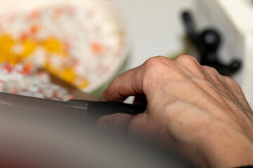 Close-up of a hand adding chopped crab sticks from a wooden board to a salad bowl. Authentic home cooking process with selective focus on the action.