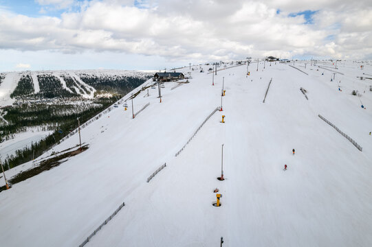 Aerial view of snow-covered slopes dotted with skiers and snow cannons under a vast, cloudy sky, Salen, Dalarna, Sweden.