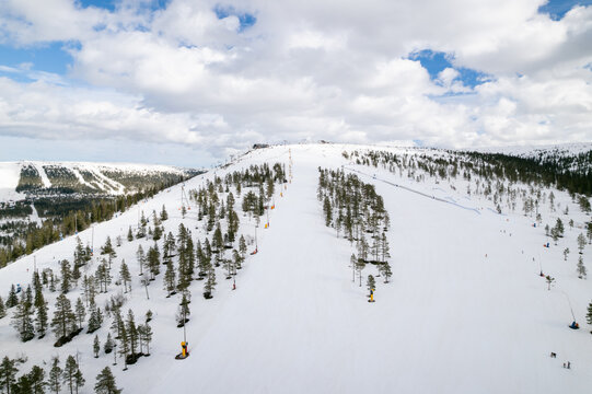Aerial view of snow-covered slopes with scattered trees under a cloudy sky, creating a serene winter landscape, Salen, Dalarnas county, Sweden.