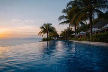 A breathtaking view of a tranquil infinity pool at sunset, surrounded by palm trees and luxury accommodations, embodies relaxation and serene beauty in nature.