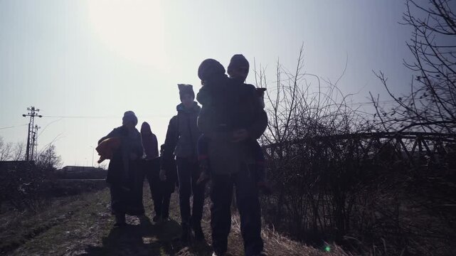 An immigrant family  in transit travels on foot, an alternative dirt road through the rural area in the dawn of the winter season