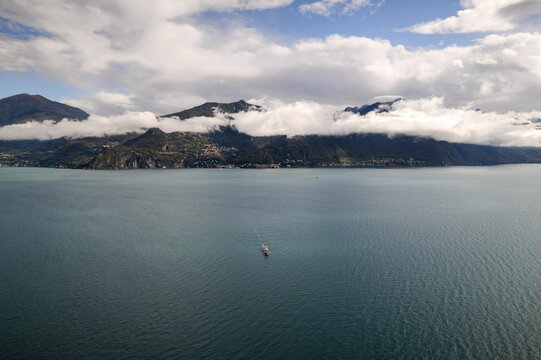 Aerial view of the serene lake's shimmering surface mirroring the sky, while mountains stand guard under a blanket of clouds, Como, Lombardy, Italy.