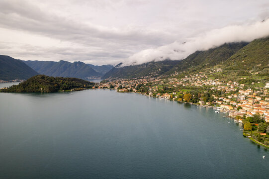 Aerial view of the tranquil lake mirroring the overcast sky, with charming settlements nestled along the water's edge and the backdrop of mountains, Azzano, Lombardy, Italy.