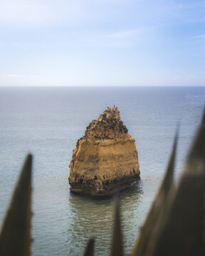 View of a majestic rock formation arises from the tranquil sea, embraced by the soft blue sky, Estrada da Marinha, Lagoa, Faro, Portugal.