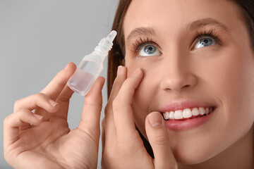 Young woman using eye drops on grey background, closeup