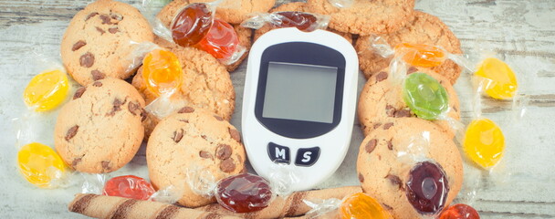 Glucose meter for checking sugar level, candies and cookies. Healthy nutrition and reduction eating sweets during diabetes