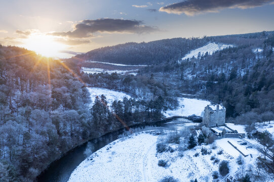 Aerial view of Neidpath Castle amidst a snowy landscape, with the River Tweed snaking through the frosty terrain under the glow of the winter sun., Peebles, Scotland, United Kingdom.