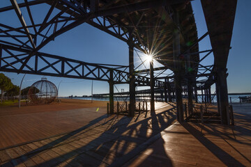 Dramatic view of the metallic Rio Tinto Pier structure in Huelva, Spain, bathed in golden sunset light and casting long shadows over the wooden boardwalk.