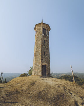 View of a stone tower rising from a hill with dry grass against a clear blue sky, a beacon of history and architecture, Canelli, Asti, Italy.