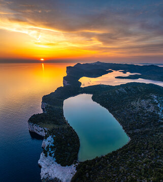 Aerial view of dramatic cliffs meet the serene lake, a symphony of blues and greens under a fiery sunset sky, Sali, Zadarska Zupanija, Croatia.