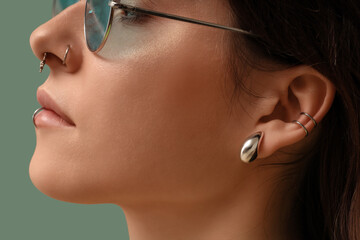 Pretty young woman in sunglasses with nose, lip and ear piercing on turquoise background, closeup